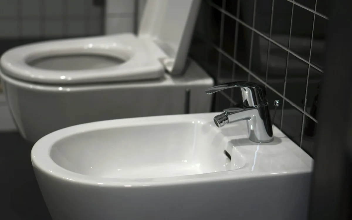 Podwieszana toaleta i bidet na tle ciemnych płytek.