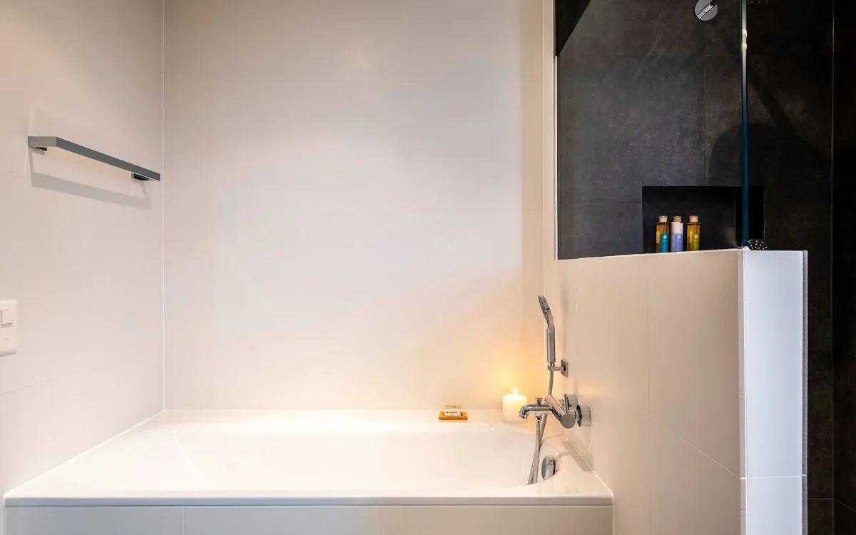 Biała prostokątna wanna w prostej, jasnej zabudowie.